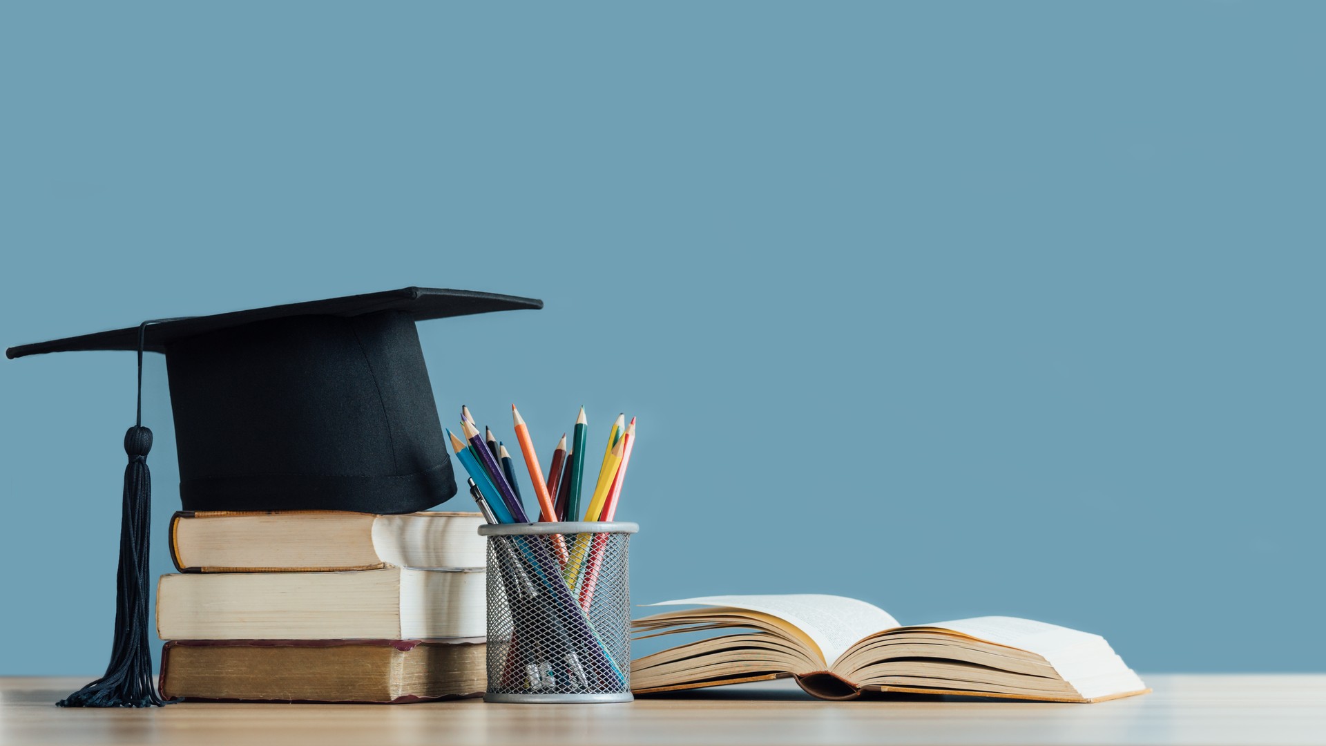 Graduation day.A mortarboard and graduation scroll on stack of books with pencils color in a pencil case on blue background.Education learning concept.